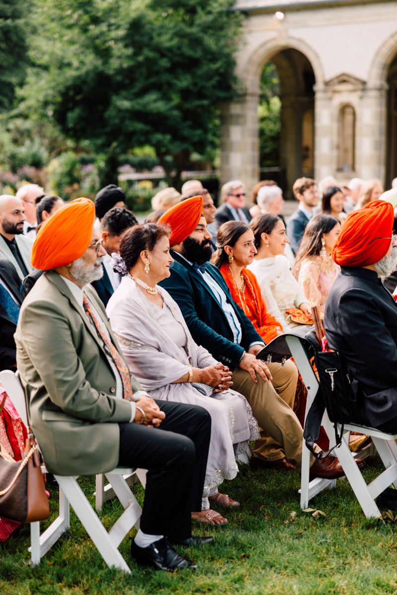 Guests seated outdoors, wearing vibrant turbans and elegant clothing, enjoying a festive event.