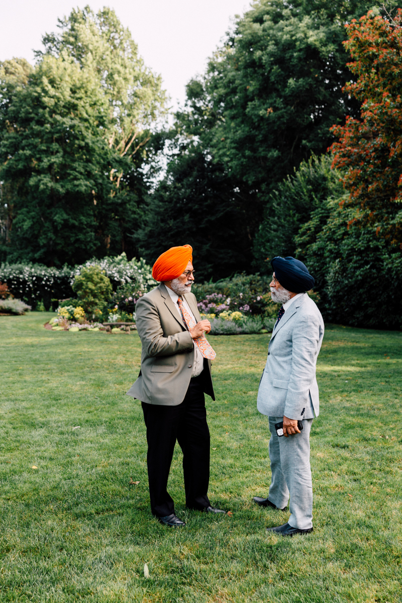Two men wearing turbans engage in conversation in a lush garden setting.