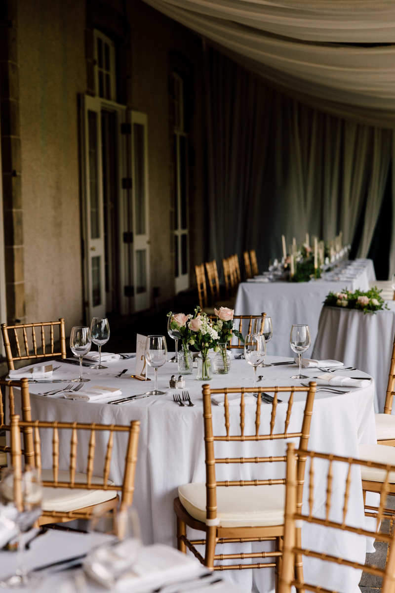 A beautifully arranged dining area featuring round tables with white tablecloths, gold chiavari chairs, and floral centerpieces, set for an elegant event.