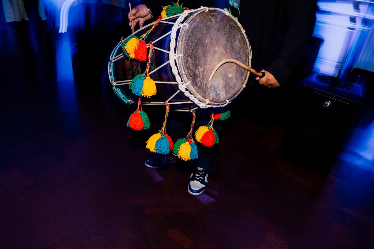 A close-up of a person playing a colorful traditional drum adorned with tassels, set against a blurred background, capturing the energy of a lively atmosphere.
