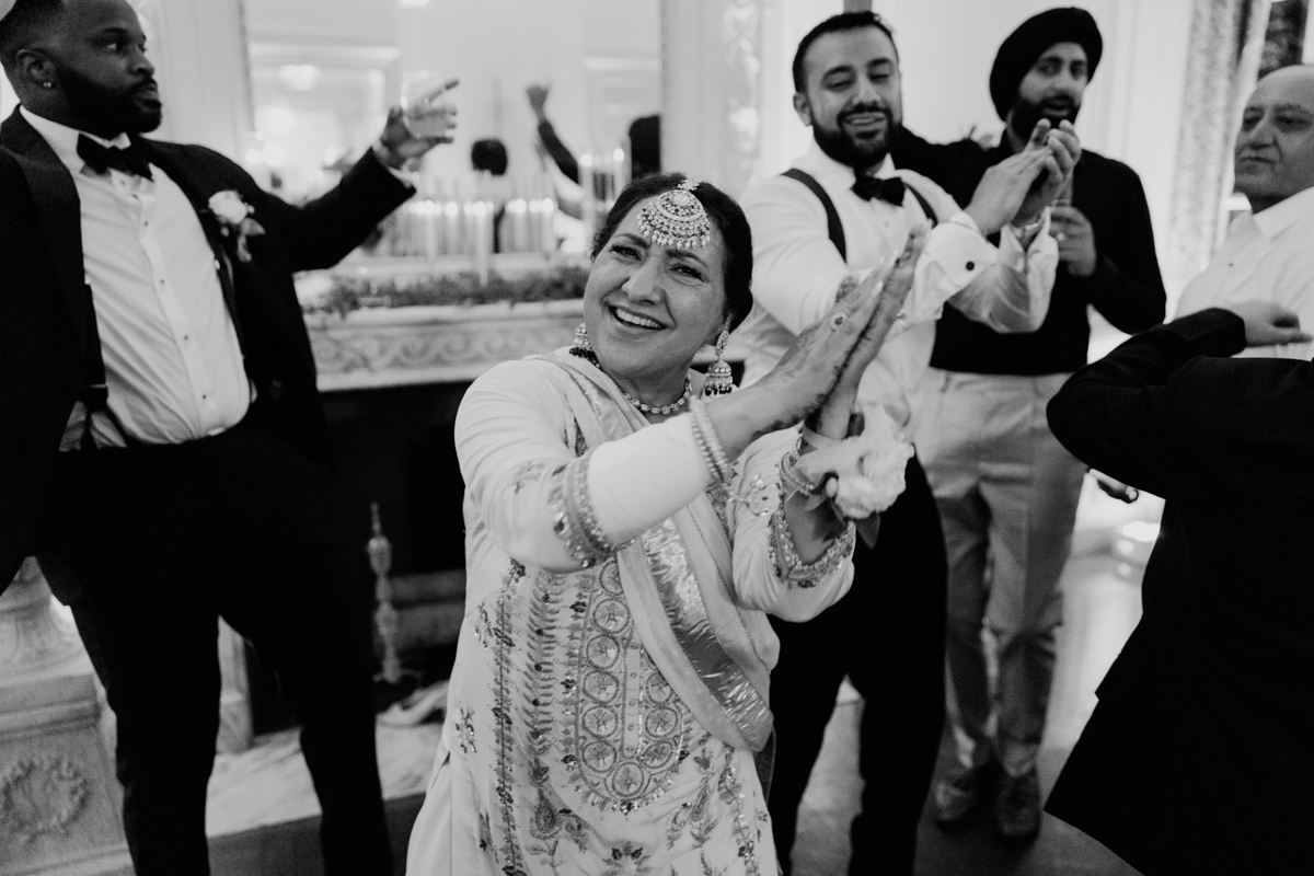 A vibrant scene featuring a smiling woman in traditional attire joyfully dancing, surrounded by elegantly dressed guests at a festive event.