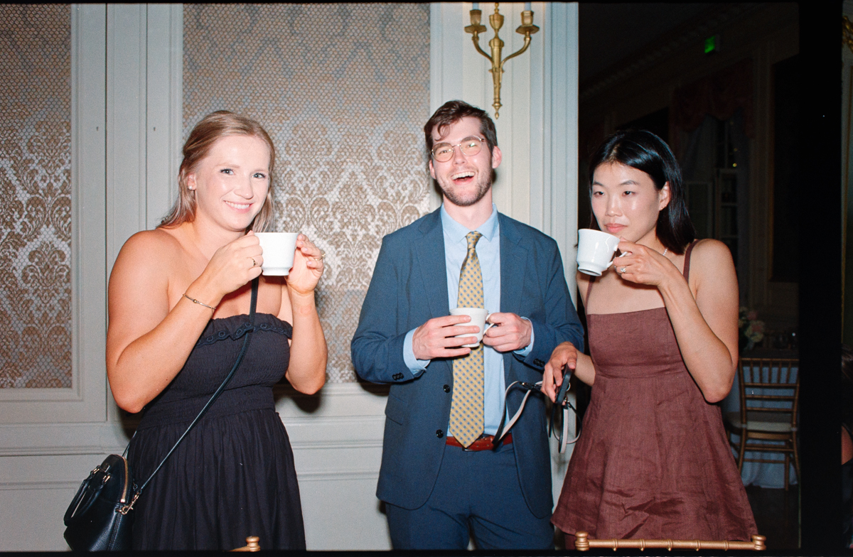 Three people enjoying coffee at a festive event, smiling and dressed elegantly.