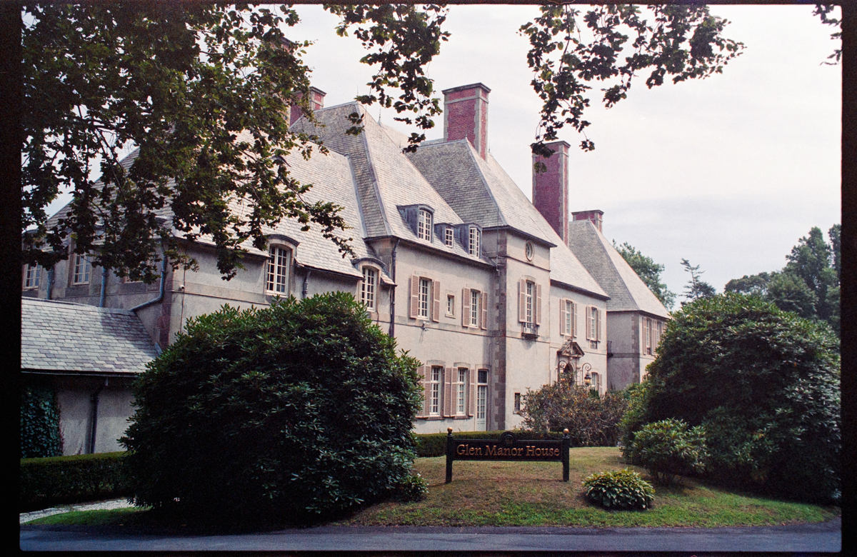A stately manor house with distinctive architecture surrounded by lush greenery and a sign marking it as Glen Manor House.