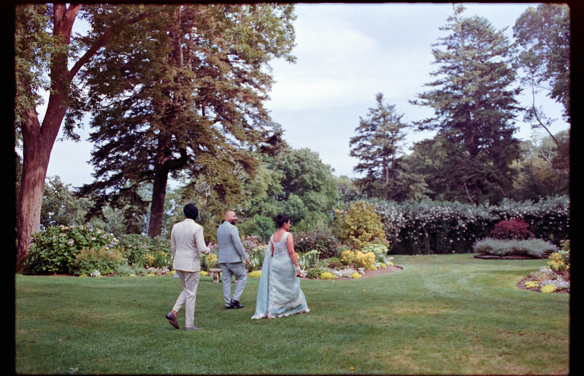 Three individuals walking through a lush garden setting during a festive occasion, surrounded by greenery and floral arrangements.