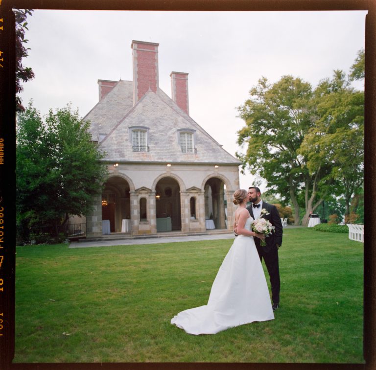 A bride and groom stand together on a lawn, embracing and gazing at each other, with the historic Glen Manor House and trees in the background—a perfect moment captured in wedding photography on a cloudy day.