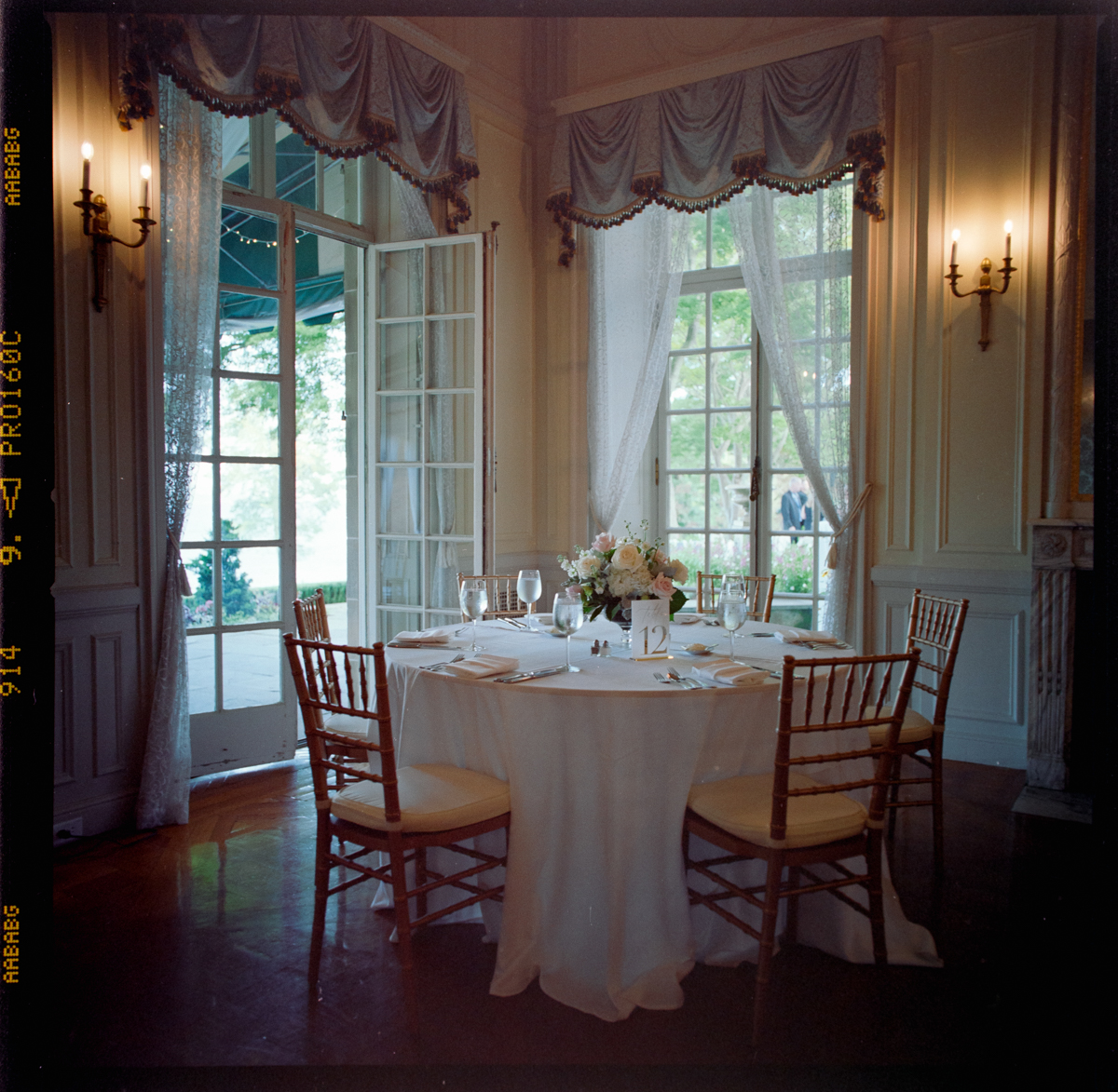 A round table set for four with elegant place settings and a floral centerpiece sits by large French doors in a sunlit, ornate room—an inviting scene perfect for Glen Manor House wedding photography.