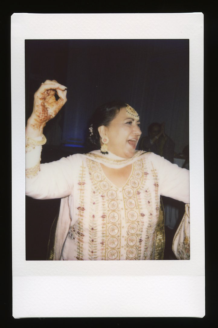 A woman in traditional South Asian attire with henna on her hand smiles and dances at a Glen Manor House Wedding, wearing a jeweled headpiece and embroidered outfit.