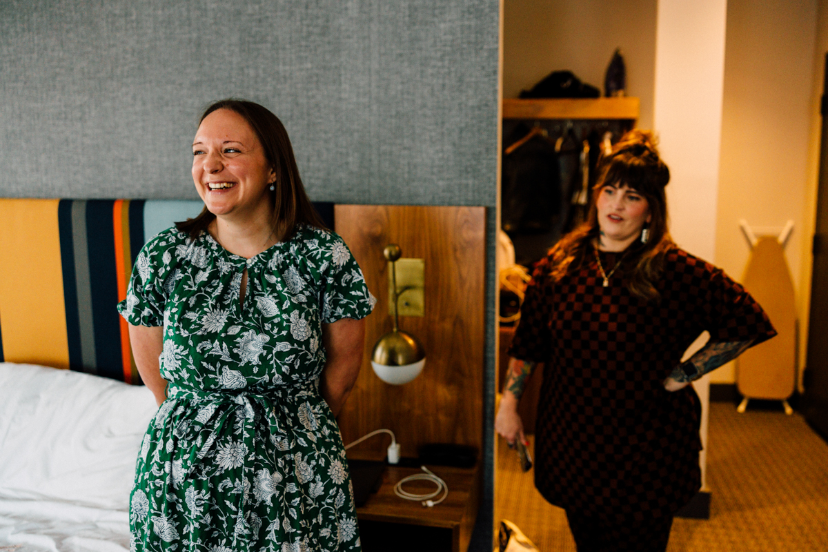 Two women share a candid moment in a stylish hotel room, showcasing a cheerful atmosphere with one woman smiling widely while the other looks on.