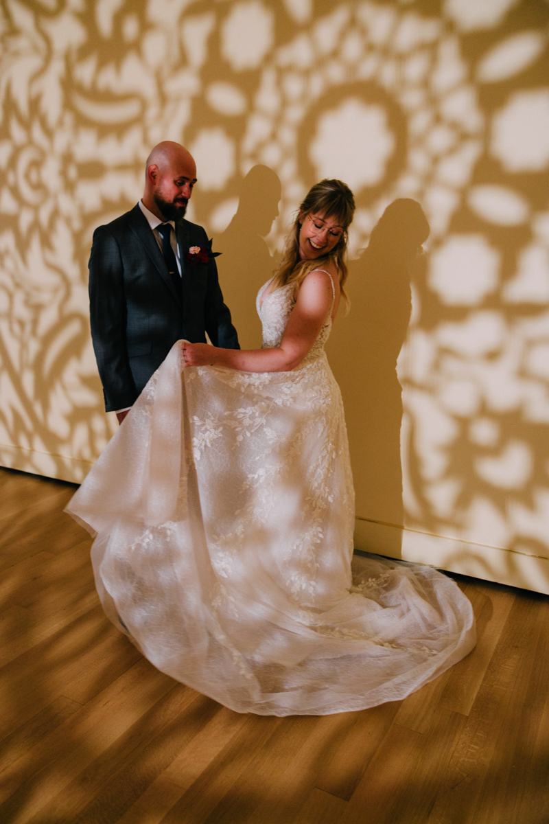 A couple shares an intimate moment, showcasing intricate shadows on the wall cast by the bride's wedding dress.