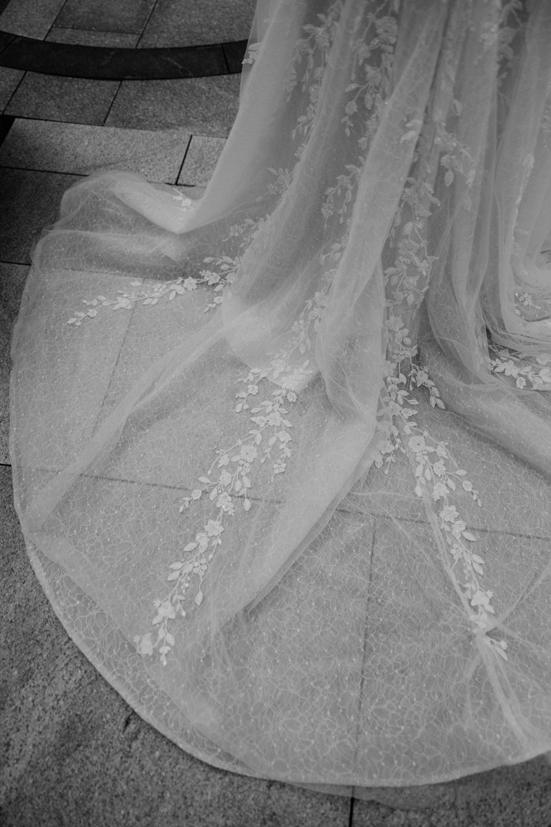 Close-up view of a delicate bridal train featuring intricate floral embroidery, displayed on textured stone flooring.
