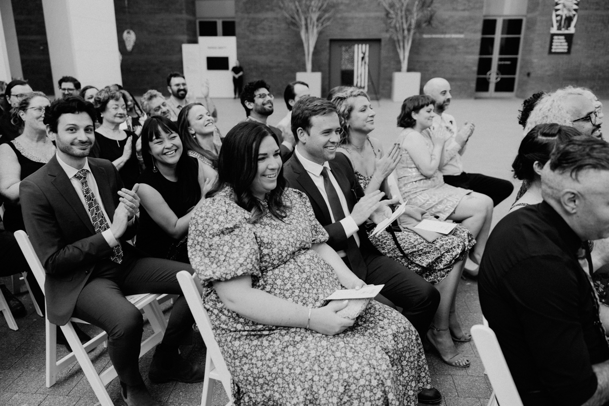 A diverse group of attendees clapping and smiling during an event, seated in an indoor venue with a warm atmosphere.