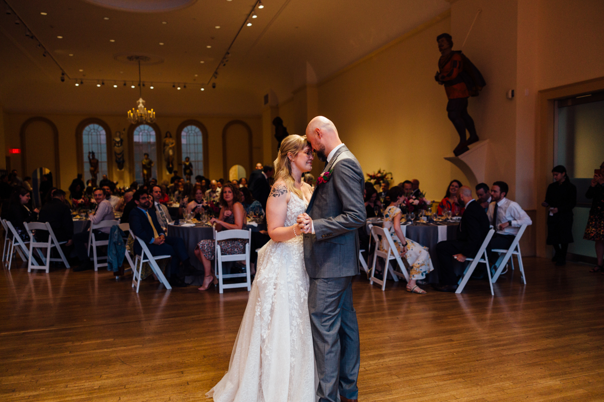 A couple shares an intimate moment during their first dance at a wedding, surrounded by guests enjoying the celebration in an elegant venue.