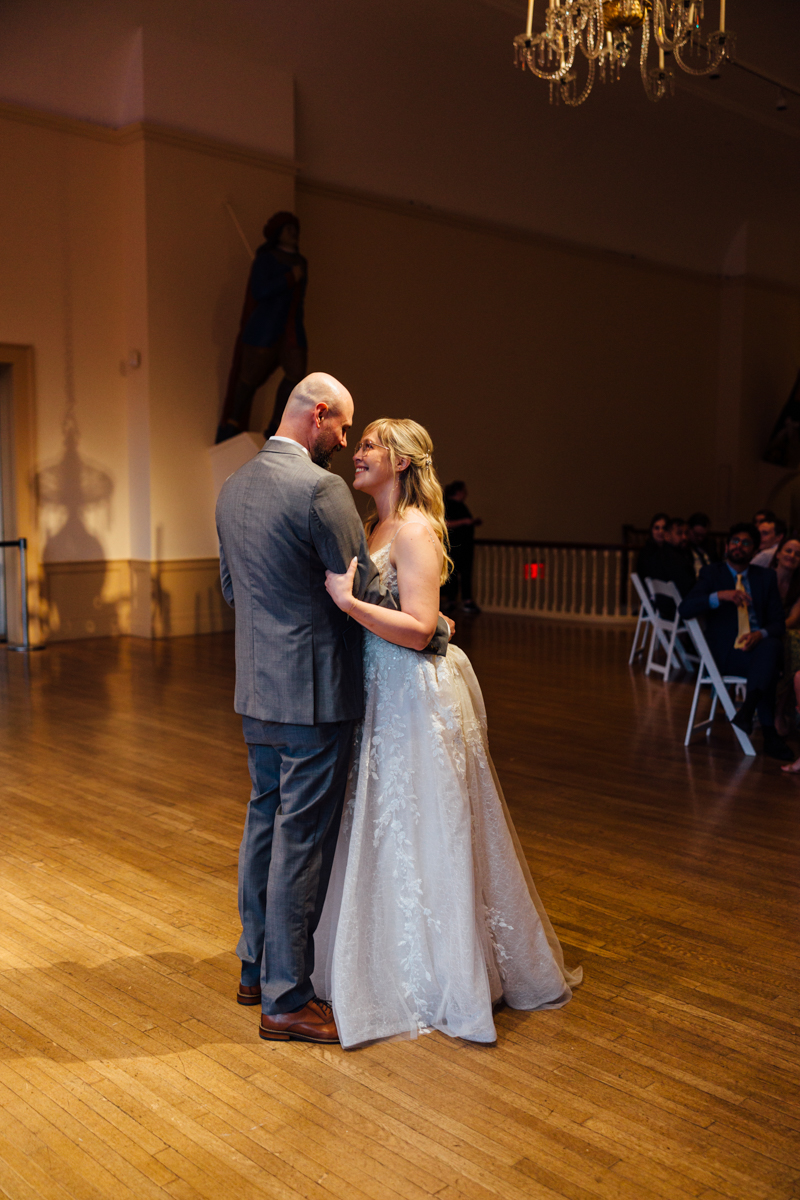 A couple sharing a joyful first dance at their wedding reception, with an elegant ballroom setting and guests in attendance.