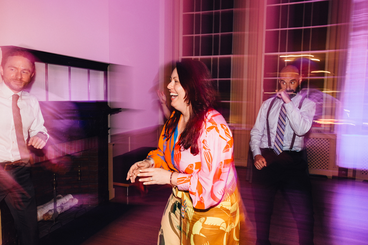 A woman laughing and dancing energetically, surrounded by others, with a blurred energetic background depicting a lively party atmosphere.