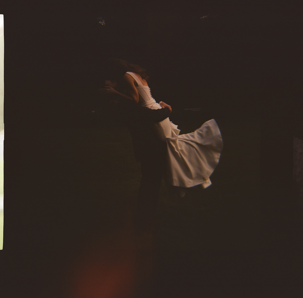 A person in a white dress is lifted in the air by another during a Seven Hills Inn wedding in Lenox MA, dim lighting and the night sky enhancing the romantic and dreamy atmosphere.
