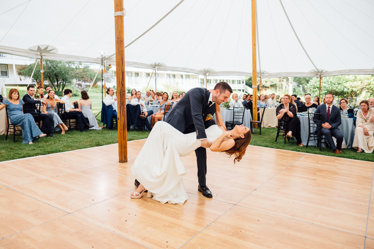 A bride and groom share a joyful dance under a white tent at their Seven Hills Inn wedding in Lenox MA, with the groom dipping the bride while wedding guests seated around the dance floor watch and smile.
