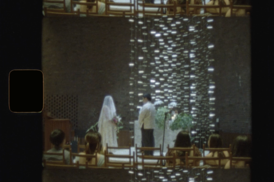 A bride and groom stand at the altar in a modern church, seen from the audience. Light filters through hanging decorations, with guests seated and watching the ceremony. The image has a soft, vintage look. It was taken on Super 8 Film by a Boston Super 8 photographer at MIT Chapel in Cambridge